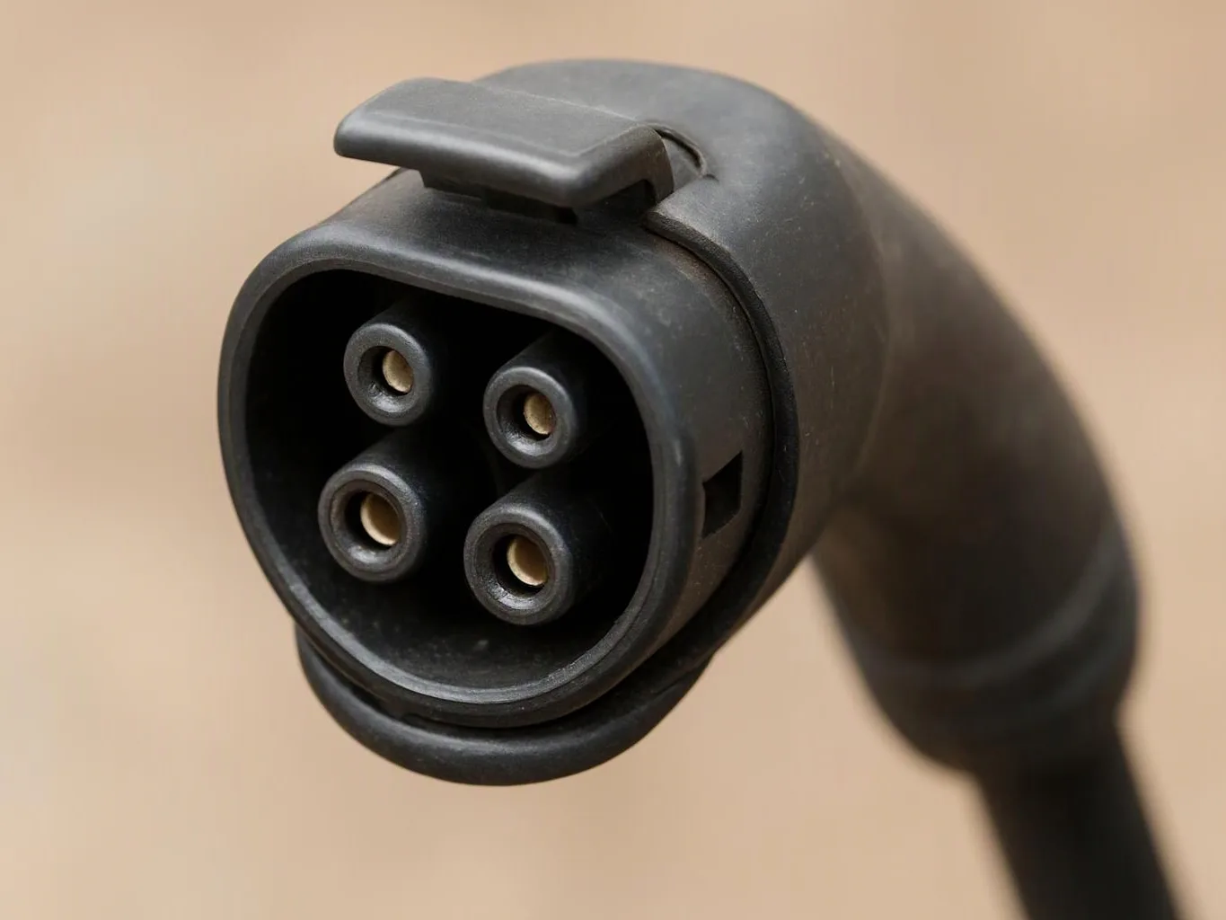 Close-up of a black electric vehicle charging connector with four round pins against a beige background