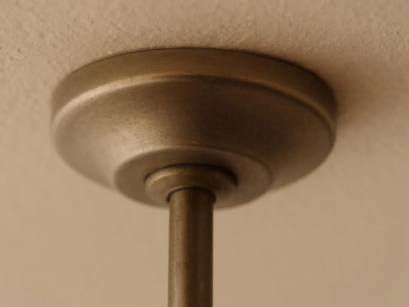 Close-up of a bronze ceiling light mount with a straight rod against a beige ceiling