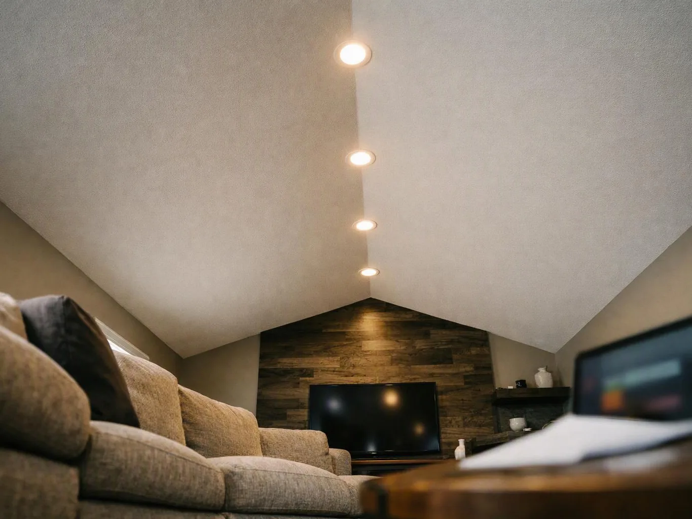 A cozy attic living room with a sofa, wall-mounted TV, and recessed ceiling lights