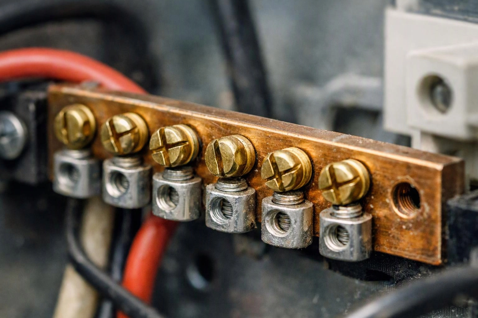 Close-up of a copper electrical terminal strip with brass screws and connected wires inside a panel